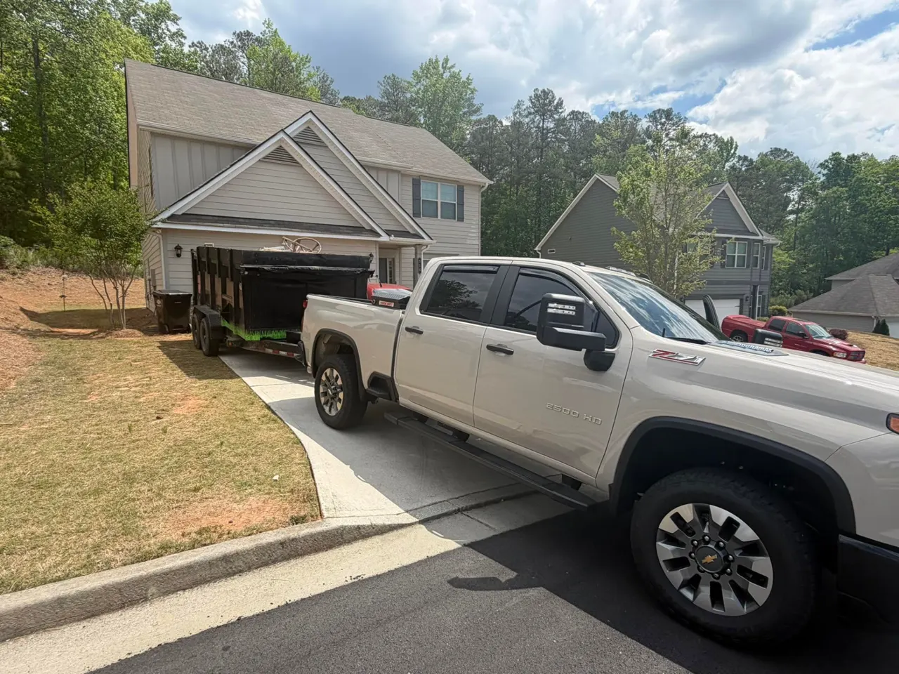 A pickup and loaded dump trailer parked in the driveway of a suburban home