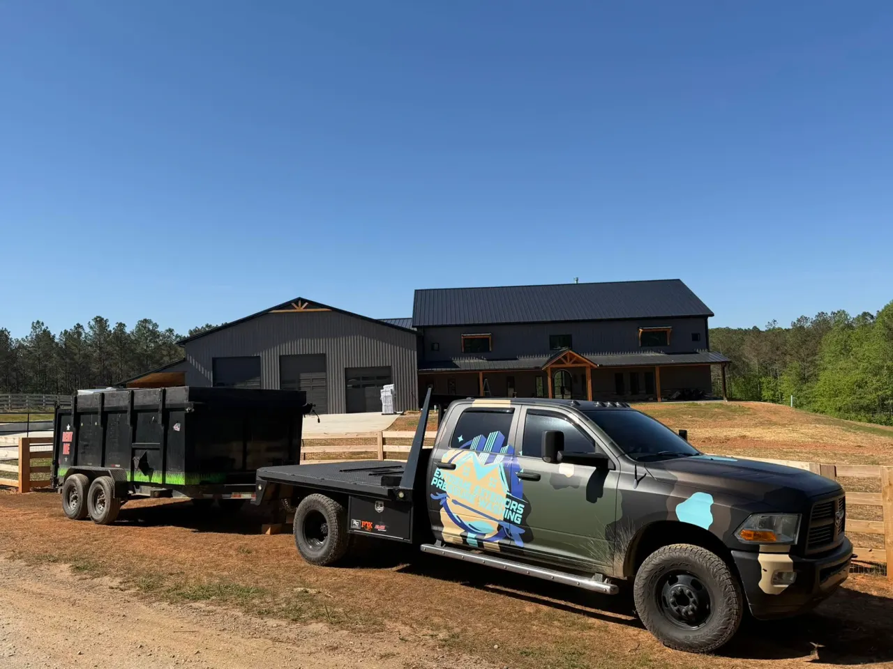A dump trailer hitched to a pickup parked in front of a large commercial building with roll-up bay doors